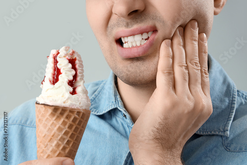 Young man with ice cream suffering from toothache on light background, closeup photo