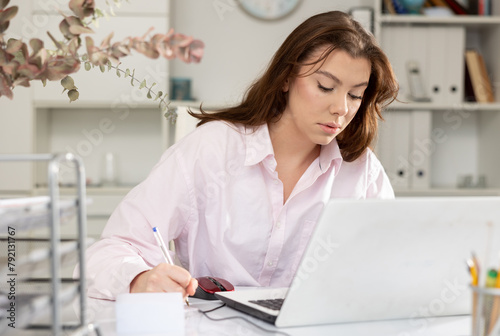 Female office worker sitting at working table and writing, doing daily paperwork.