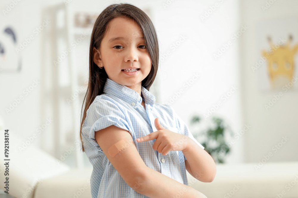 Little Asian girl pointing at applied patch after vaccination in clinic Little Asian girl pointing at applied patch after vaccination in clinic