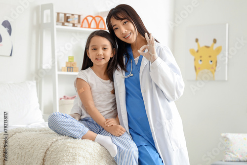 Female Asian doctor showing OK with little girl after vaccination in clinic