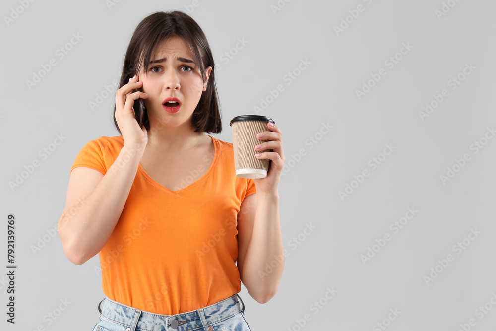 Young stressed woman with cup of coffee talking by mobile phone on grey background. Stress Awareness Month - obrazy, fototapety, plakaty 