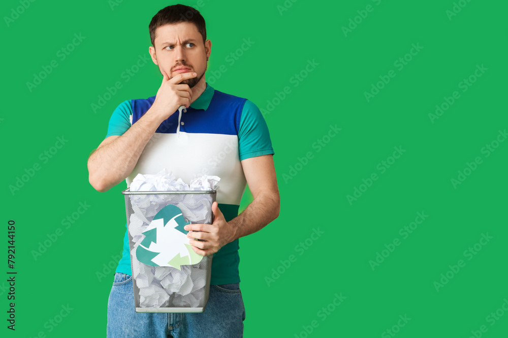 Thoughtful young man holding trash bin with recycling logo on green background. Ecology concept Thoughtful young man holding trash bin with recycling logo on green background. Ecology concept