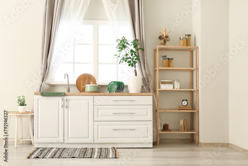 Interior of stylish kitchen with white counters, window, sink and shelving unit