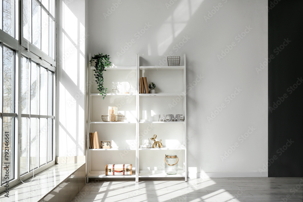 Fototapeta premium Shelving unit, window and houseplants near white wall in light room