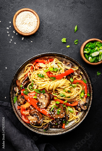 Vegan stir fry noodles with red paprika, champignons, green onion and sesame seeds with ginger, garlic and soy sauce.. Black table background, top view