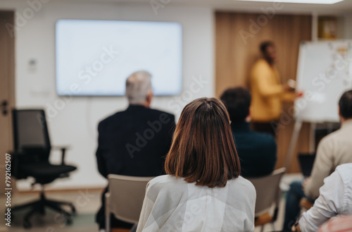 Attentive businesspeople watching a presenter in a corporate training session in a well-lit conference room with a whiteboard.