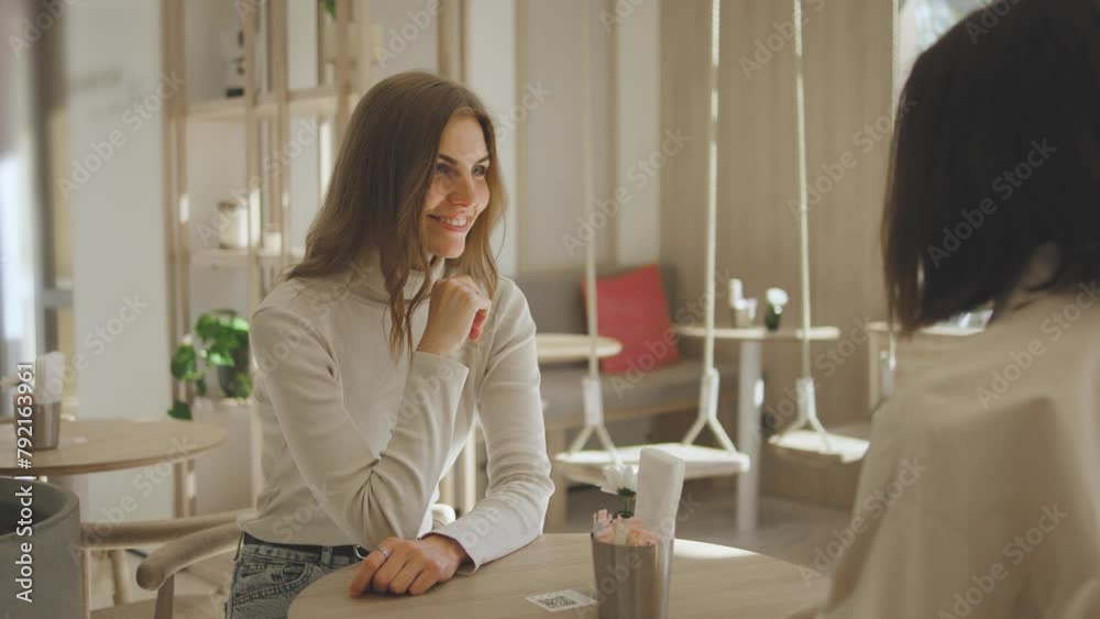 Two beautiful young women are sitting in a cafe and talking to each other. Two friends met in a cafe and are talking