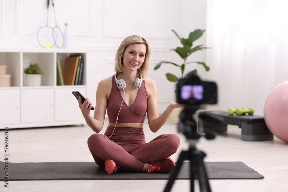 Smiling sports blogger recording fitness lesson with camera at home Smiling sports blogger recording fitness lesson with camera at home