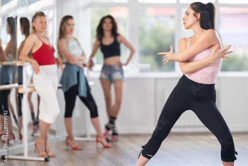 Expressive young adult woman demonstrating fluid sensual movements of modern vogue dance, blending femininity and style, to attentive group of female participants in choreographic studio....