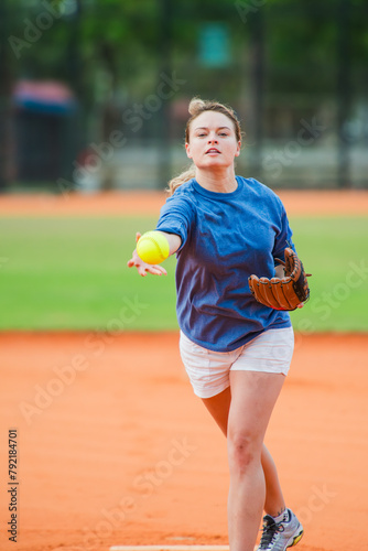 Young woman pitching fluorescent yellow softball on field during game. © Eric Hood