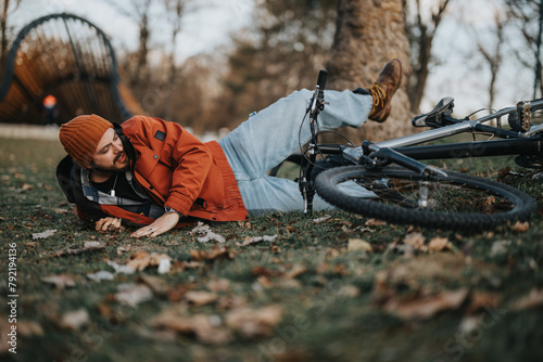 Casual young man with a hipster style falls from his bike onto the grass in an urban park setting. photo