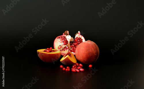 Broken ripe pomegranate fruit with seeds and pieces of peach on a black abstract background.