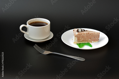 A piece of mint cream cheesecake on a plate, a fork and a cup of hot black coffee.