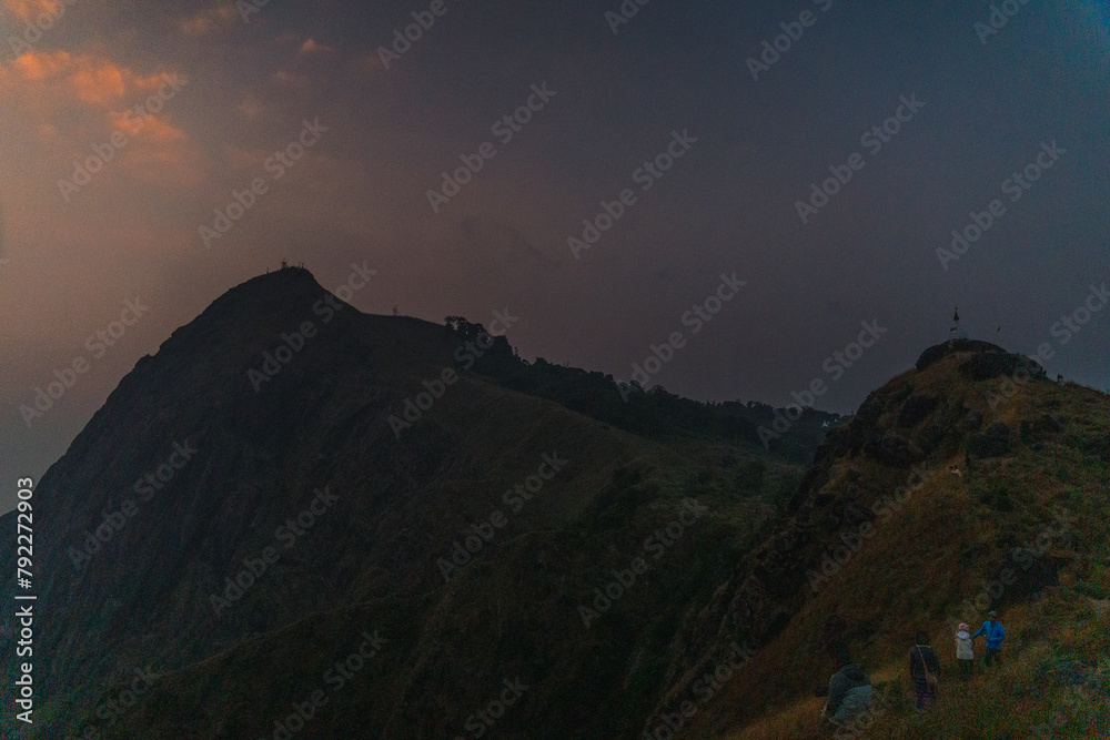 Naklejka premium A mountain range with a cloudy sky and a person standing on top of it