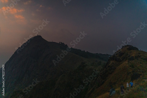 A mountain range with a cloudy sky and a person standing on top of it