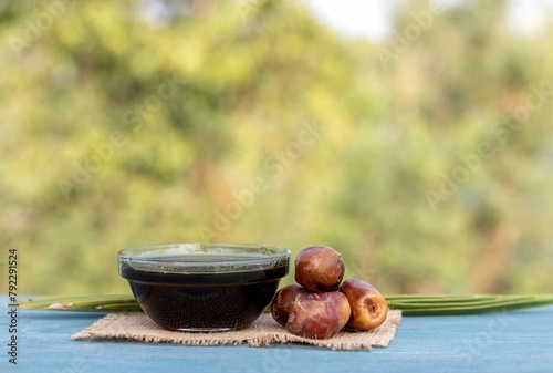 Date Palm Liquid Jaggery in a Glass Bowl or Phoenix Dactylifera Fruit with Leaves on Burlap Fabric Isolated on Wooden Table with Copy Space