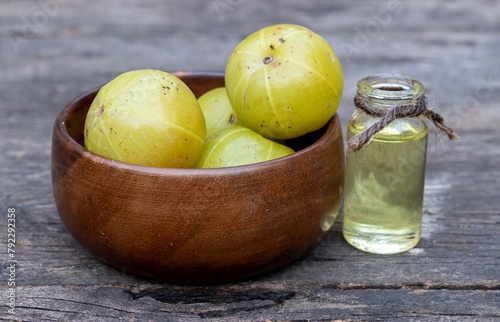 Amla Oil in a Glass Bottle or Indian Gooseberry Fruit or Amla Fruit in a Wooden Bowl Isolated on Wooden Background with Copy Space, Also Known as Emblica Myrobalan or Phyllanthus Emblica