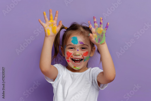 A happy girl with paint on her hands and face  smiling while posing for the camera against light purple background  wearing white tshirt