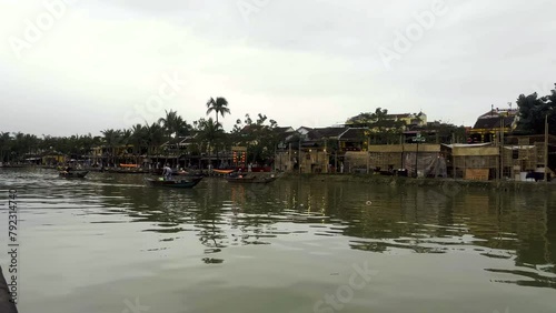 Boats sailing on a calm river. Boats on the Thu Bon River with palm trees and buildings in the background. Hoi An ancient town. UNESCO World Heritage site. Hoi An, Vietnam. photo