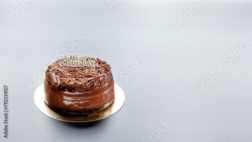 A dark black forest chocolate cake with a Happy Birthday sign sits on a black background