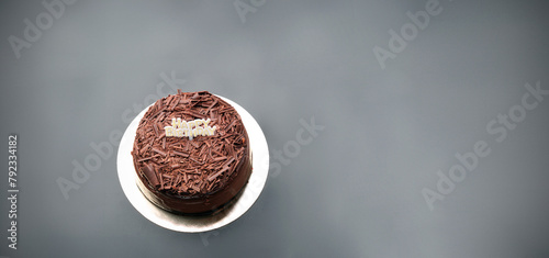 A dark black forest chocolate cake with a Happy Birthday sign sits on a black background