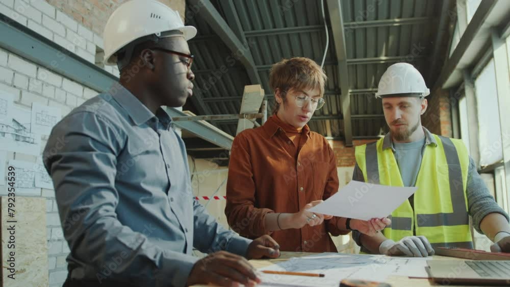 African American architect and Caucasian engineer wearing hardhat discussing building plan on paper with female client visiting construction site African American architect and Caucasian engineer wearing hardhat discussing building plan on paper with female client visiting construction site