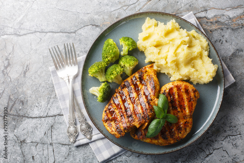 portion of grilled chicken breast with a side dish of mashed potatoes and broccoli close-up in a plate on the table. Horizontal top view from above