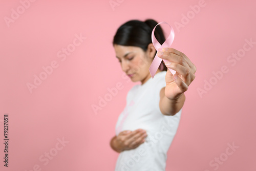 Selective focus of pink ribbon held by a woman on isolated pink background. breast cancer awareness concept