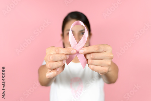 selective focus of woman hands holding a red ribbon on an isolated pink background