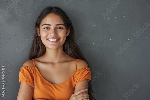 Smiling young Latin woman with crossed arms standing against grey wall