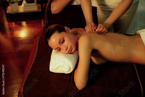 Caucasian couple customer enjoying relaxing anti-stress spa massage and pampering with beauty skin recreation leisure in warm candle lighting ambient salon spa at luxury resort or hotel. Quiescent