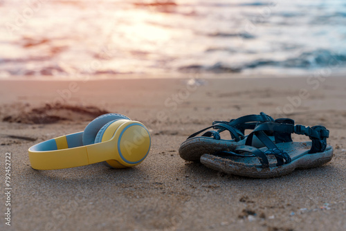 Headphones and sandals on the beach near the sea at sunset. Take music or book on a journey, listen to the music, audiobook, podcast everywhere. Copy space