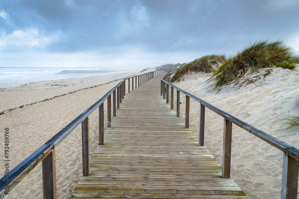 A wooden pedestrian walkway with railings runs along the oceanfront dunes.