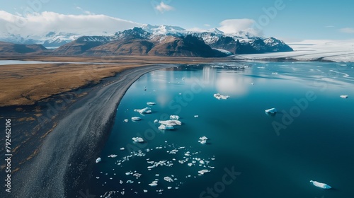 aerial view of the Jökulsárlón glacier lagoon, where shimmering icebergs float serenely amidst the glacial waters, framed by black sand beaches and snow-capped mountains
