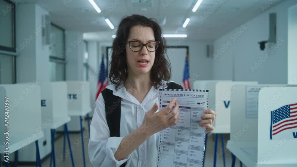 American female citizen speaks on camera, shows paper ballot, calls for voting. National Election Day in the United States. Voting booths at polling place. Civic duty and patriotism concept. Portrait.