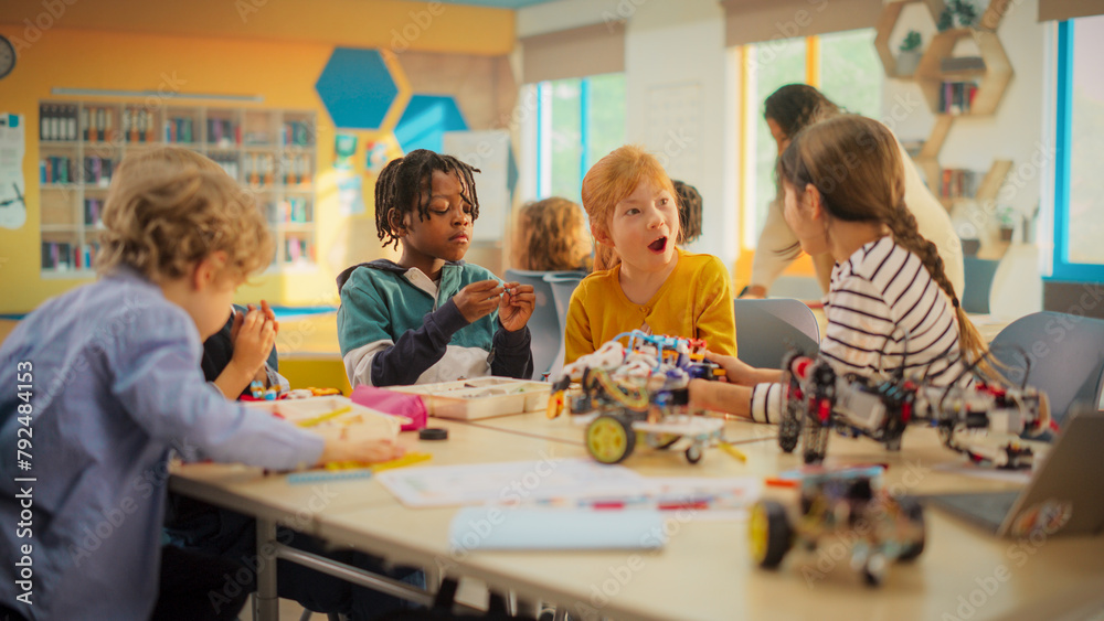 Elementary School Pupils Sitting Behind a Table in a Group, Building a Robot Hand Project for a Science and Technology Fair. Young Boys and Girls Wish to Become Engineers in Robotics Elementary School Pupils Sitting Behind a Table in a Group, Building a Robot Hand Project for a Science and Technology Fair. Young Boys and Girls Wish to Become Engineers in Robotics
