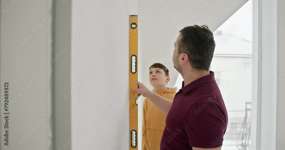 Father and his young son engaged in home renovation. The family is actively involved in repair, painting the walls white and taking measurements. Family bonding during a DIY home renovation project Father and his young son engaged in home renovation. The family is actively involved in repair, painting the walls white and taking measurements. Family bonding during a DIY home renovation project