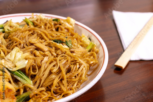 Fried noodle with chicken and vegetables in a white bowl on a wooden table. After edits.