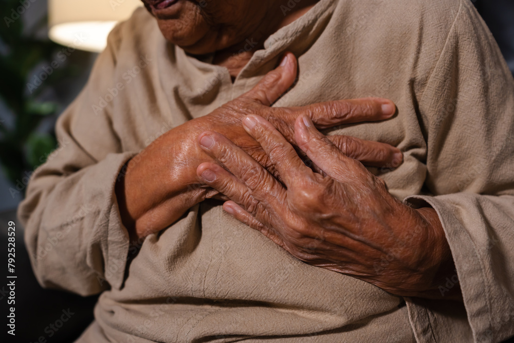 Fototapeta premium close up senior woman suffering from bad pain in her chest heart while sitting on sofa in the living room at night