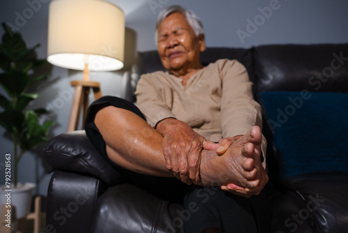senior woman suffering from foot and ankle pain while sitting on sofa in the living room at night