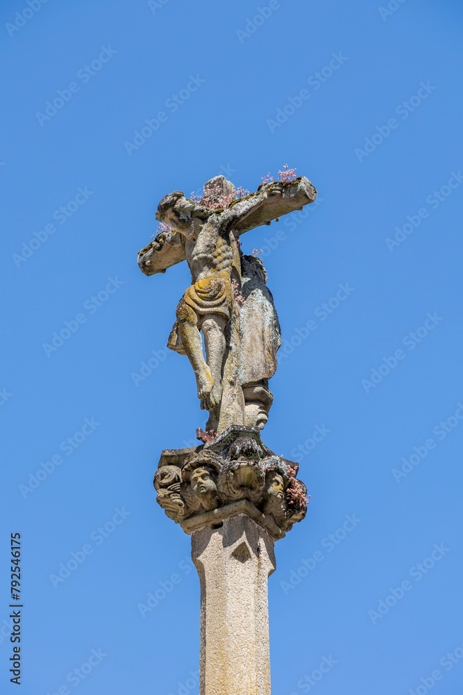 A close-up of a weathered Jesus Christ statue on a cross with intricate details and sky in the background, capturing the essence of faith and history