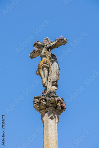 A close-up of a weathered Jesus Christ statue on a cross with intricate details and sky in the background, capturing the essence of faith and history