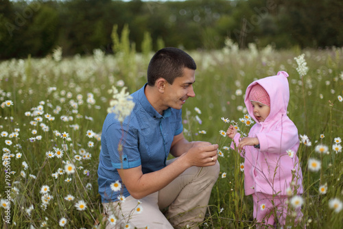 Smiling cheerful brunette Caucasian father and baby girl having fun on meadow among chamomile flowers man with infant daughter enjoying warm summer day