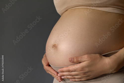 Pregnancy time. Expectation time. Unknown young adult pregnant woman touching big naked belly with hands showing shape, copy space for advertisement area