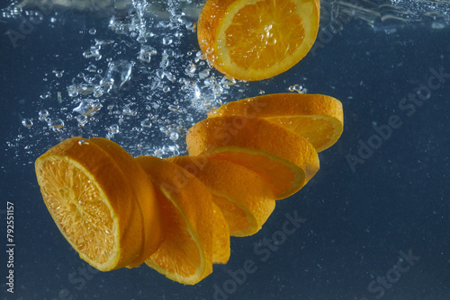 Fresh orange slicers falling in water with splashing isolated over dark blue background, copy space
