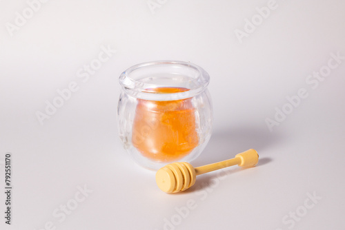 A glass of liquid honey with a honey dipper on white background