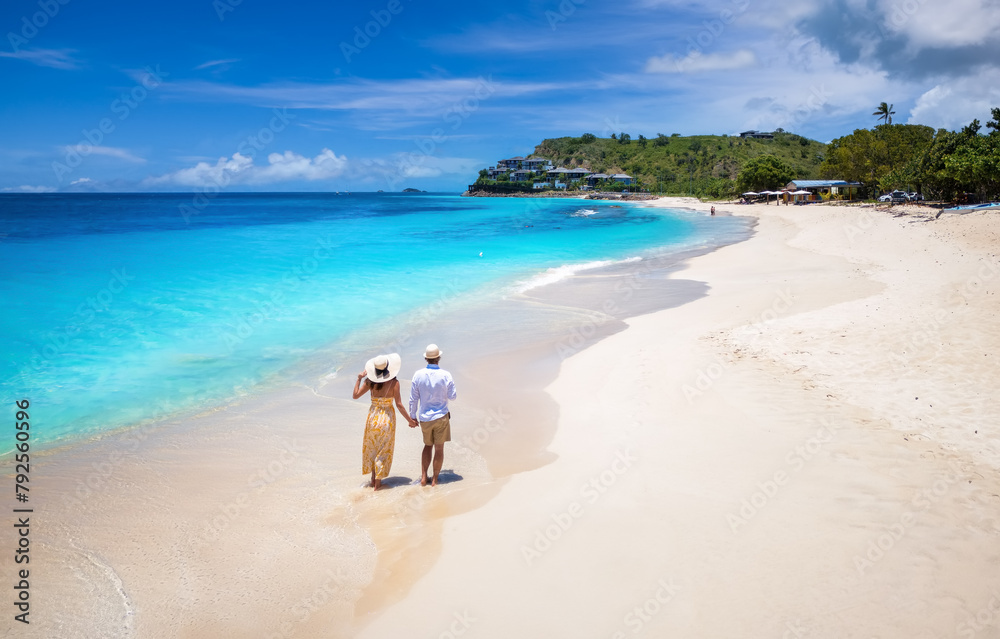 Elevated view of a couple walking down the beuatiful Darkwood beach with turquoise sea in the Caribbean, Antigua and Barbuda islands