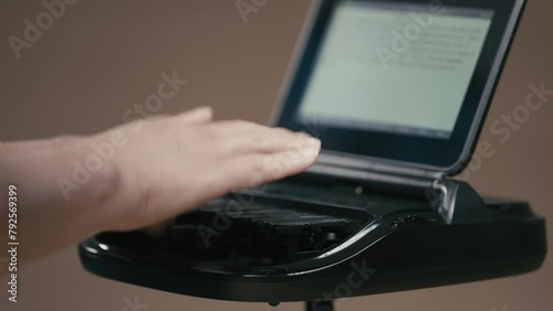 Court reporter typing on stenographer machine with out of focus screen in background photo