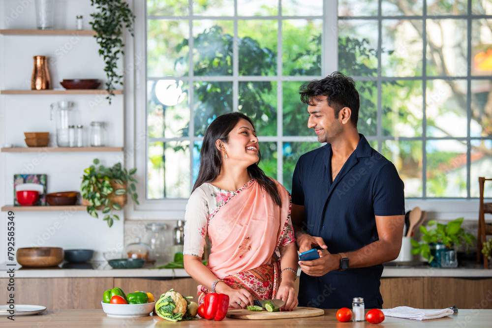 Indian asian smart young couple using smartphone in modern kitchen Indian asian smart young couple using smartphone in modern kitchen