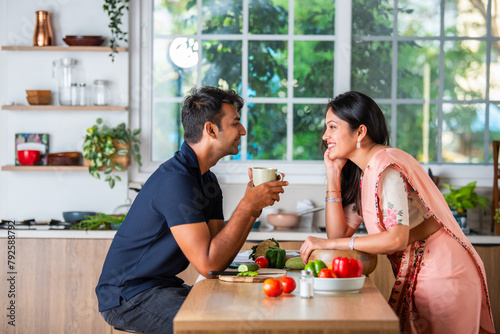Indian asian pretty young couple having coffee or tea in the mug in kitchen